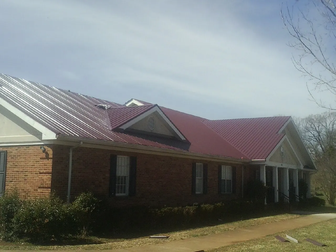Red metal roof with gabled entries on a long brick building, from a Hail Damage Roof Repair job in Monroeville