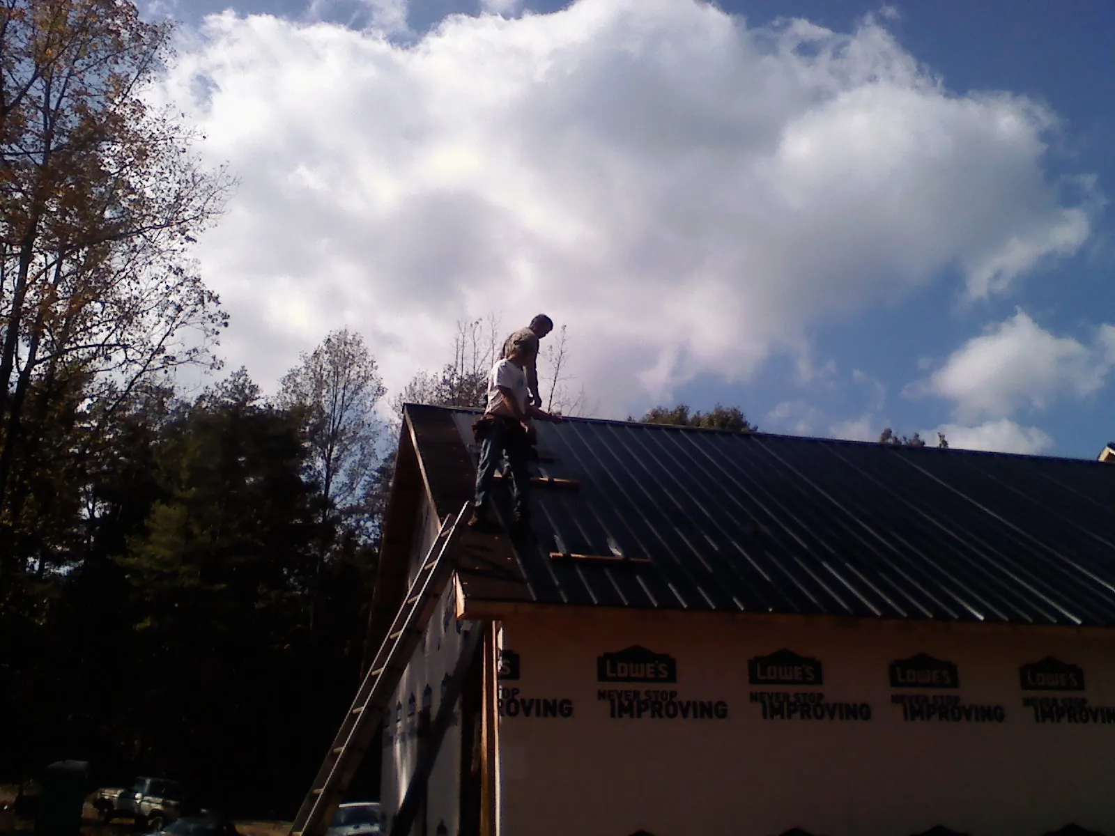 Roofer fastening dark metal panels high against a cloudy sky, from a Roof Inspection job in Monroeville